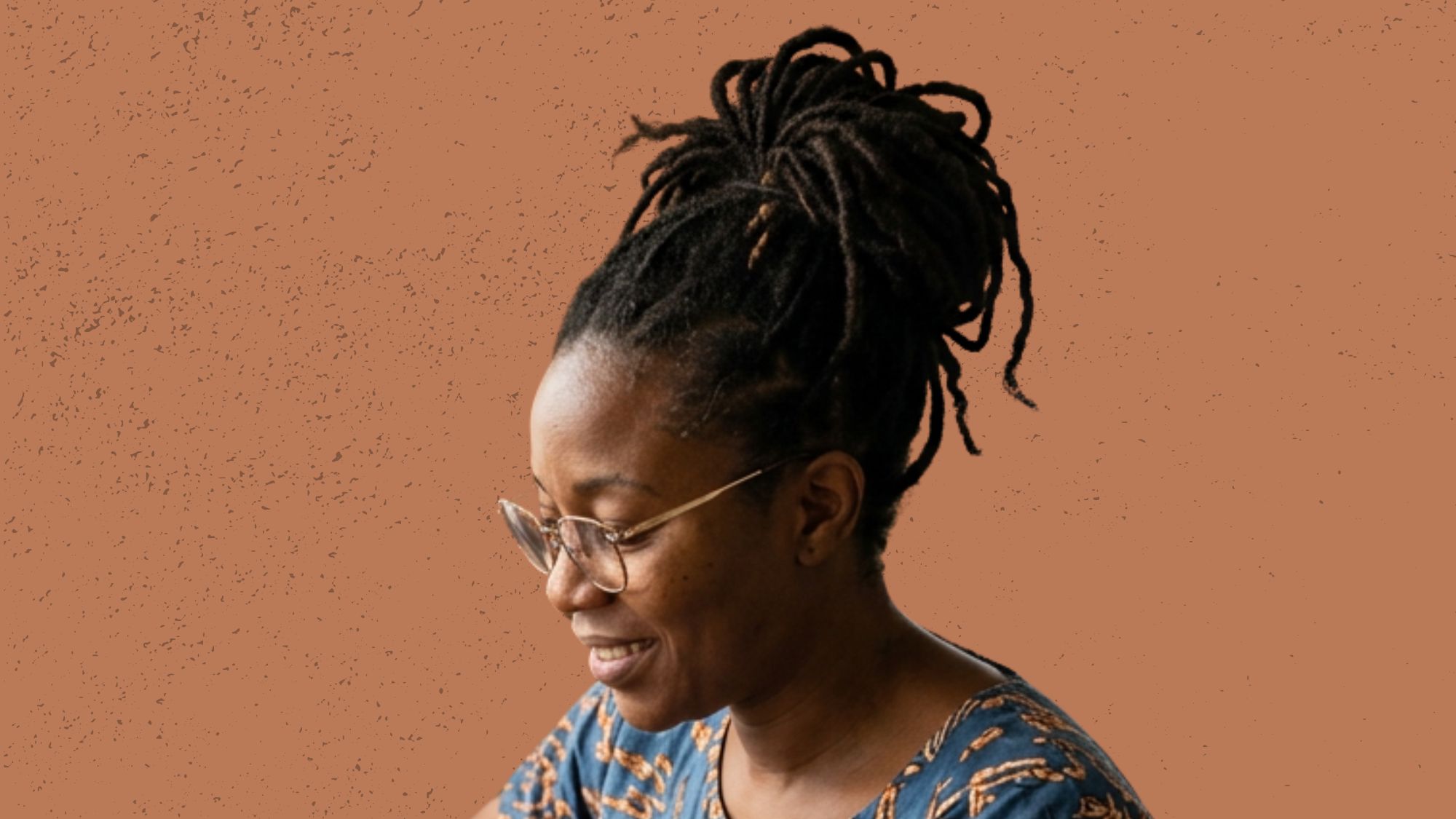 Woman writing her mature locs retwist schedule in a notebook at a vanity with jojoba oil and rose water spray bottle nearby