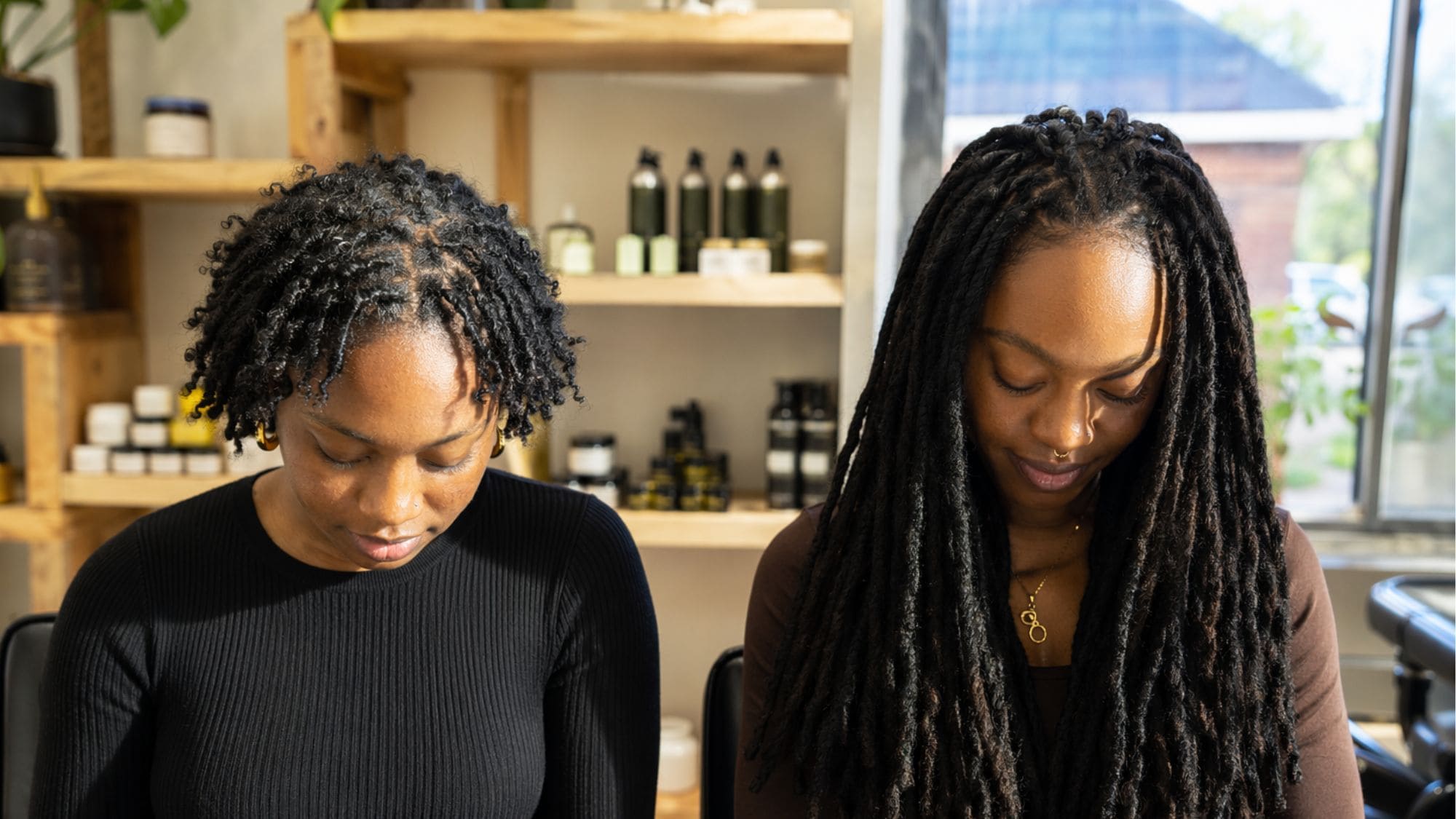 Two women in a natural hair salon comparing short starter locs and long fully mature locs side by side